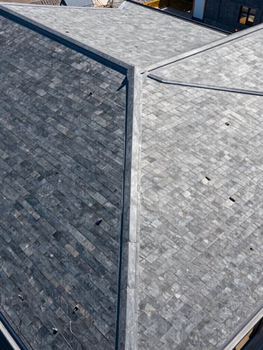Wide-angle architectural drone shot of a flawless slate-gray roof, bright midday sun, high-contrast crisp shadows, sharp detail
