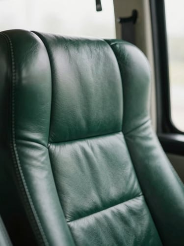 Close-up detail of a premium hand-stitched dark leather bus seat, soft natural window light, deep green tones, sharp focus, 35mm