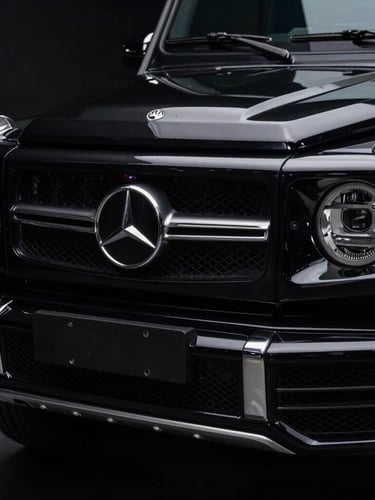Low-key dramatic studio lighting on a black Mercedes G-Class grille, sharp metallic reflections, high contrast dark environment