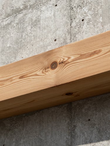 Tactile close-up of raw timber beams meeting a board-formed concrete wall, high-contrast side lighting, real shadows