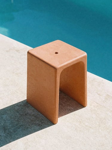 Low-angle architectural shot of a terracotta Monobloc stool on sun-drenched concrete by a deep blue pool, sharp midday shadows, matte polymer texture, 35mm film