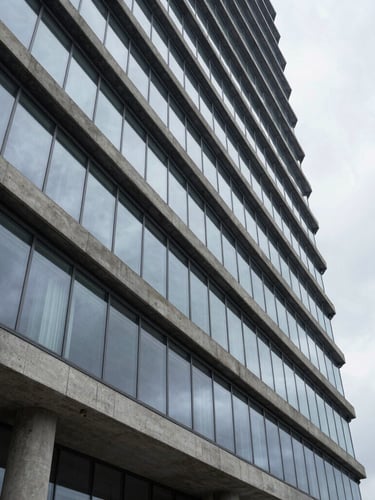 Wide architectural angle of a modern concrete and glass high-rise facade, clean geometric lines, diffused overcast daylight, reflecting a quiet sky.