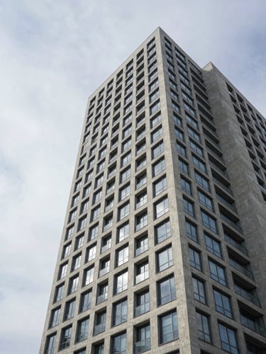 Wide architectural angle of a modern concrete high-rise with glass facades under soft, diffused overcast daylight, clean lines, negative space on the left.