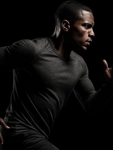 High-contrast studio photograph of an athlete in motion wearing a custom-branded charcoal training top, dramatic side lighting, sharp details