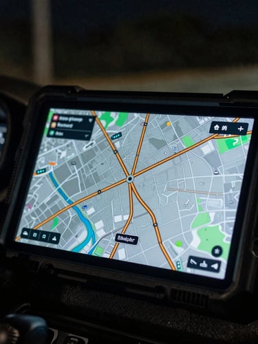 Close-up of a rugged tactical tablet displaying a high-contrast GPS route map with amber lines, dark dashboard of a vehicle at night, cinematic lighting