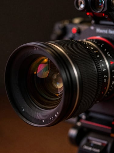 Cinematic film photography, close-up of a high-end anamorphic camera lens on a dark production set, dramatic low-key lighting with red practical accents, shallow depth of field, 35mm grain