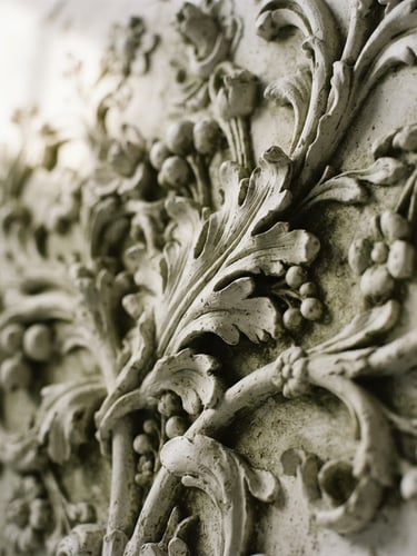 Macro detail shot of carved white plaster relief, soft natural window light casting deep shadows, warm editorial art photography, muted olive tones