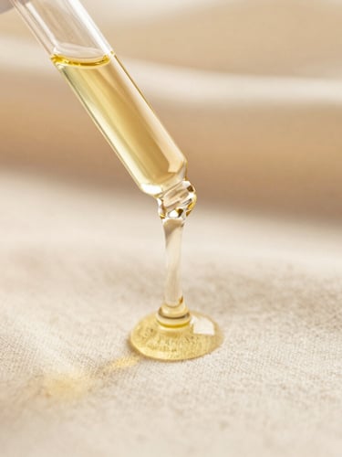 Macro detail shot of botanical oil dripping from a glass dropper onto soft cream linen, warm golden-hour glow, shallow depth of field, 35mm editorial photography
