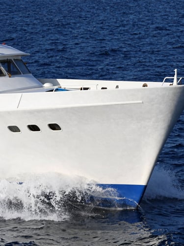Dynamic low-angle shot of the bow of Aurora Fortunada cutting through deep blue water, crisp white hull, bright afternoon sun, water spraying from the hull.