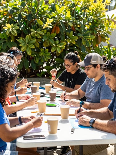 Vibrant outdoor community workshop in South Florida, diverse people collaborating around a table, bright natural sunlight, fresh green foliage in background, 35mm