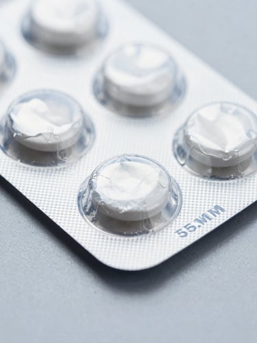 Macro close-up of sealed silver medicine blister packaging on a sterile slate grey surface, clinical blue lighting, sharp focus, 35mm