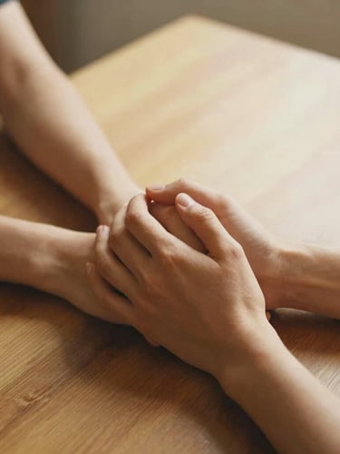 Warm editorial photograph of hands holding hands on a wooden table, soft golden-hour ambient glow, nostalgic muted tones, close-up detail