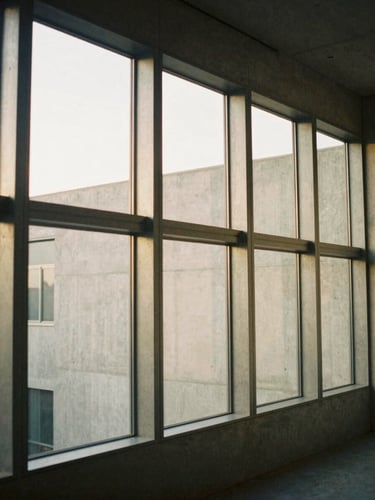 Architectural interior photography of a residential steel frame integrated with concrete walls, soft natural afternoon light filtering through large empty window openings, muted warm neutral tones, medium format film.