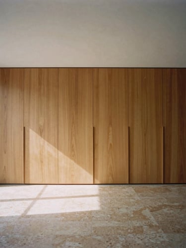 Straight-on architectural elevation of a minimalist residential living room, custom walnut millwork, natural light casting long shadows across warm travertine floors, medium format film