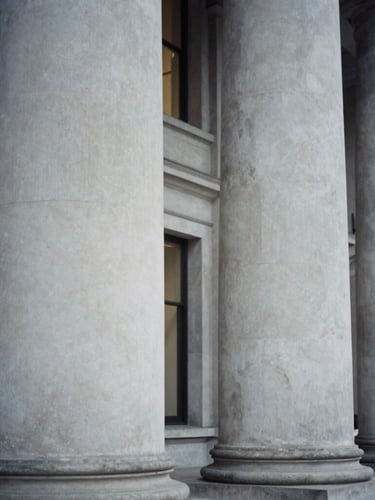 Close-up editorial corporate photograph of structured Portland stone pillars in London, soft interior window light, desaturated cool tones, architectural framing, 35mm film.