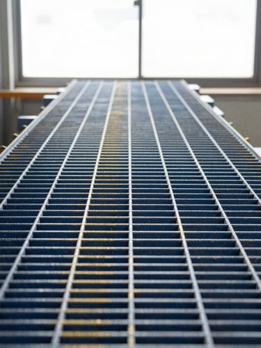 Straight-on profile of a heavy-duty industrial fiberglass structural grating, deep blue and golden yellow resin-matrix formulation, crisp factory window light
