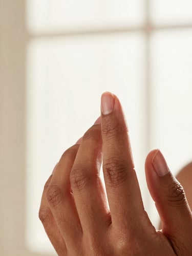 Close-up of a person of color applying cream blush with their fingertips, soft diffused window light, natural skin texture visible, warm terracotta tones, shallow depth of field