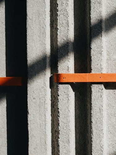 Extreme close-up of thick, textured cotton fabric seams against a rough concrete background, harsh architectural shadows, desaturated tones with a sharp orange accent.