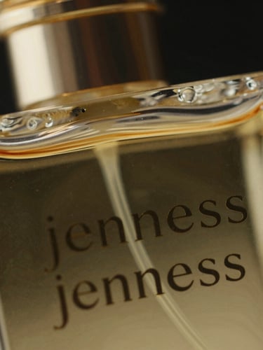 Extreme close-up macro shot of the Jenness perfume bottle glass texture, strong directional gold rim lights, pitch-black background.