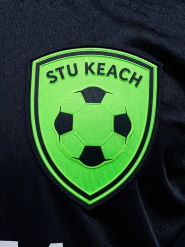 high-contrast athletic photography of a neon green heat-applied football club crest on a dark textured player-version jersey, dramatic stadium lighting, rich saturated colors, sharp focus, 35mm