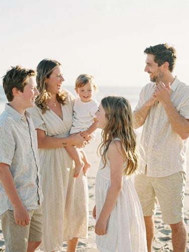 A family laughing together on a warm sandy beach, wearing light linen clothing, candid medium shot, soft golden-hour light, shallow depth of field.