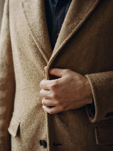Close-up of a vintage wool coat texture, with a hand gently feeling the fabric, warm natural window light, muted nostalgic tones, 35mm film aesthetic.