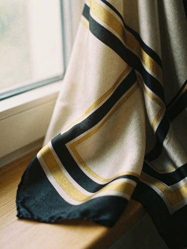 Close-up of a structured silk scarf with gold and black geometric patterns, draped over wood, soft window light.