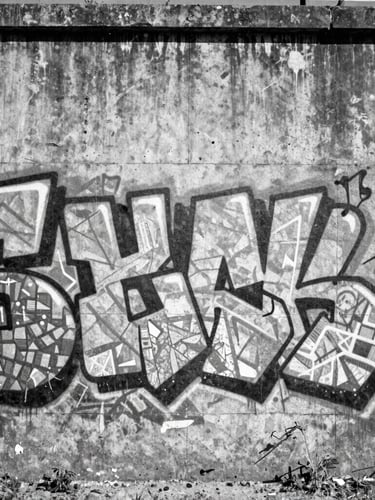 Gritty black and white portrait of a concrete spillway covered in abstract geometric graffiti, harsh midday sun, deep shadows, raw architectural texture.