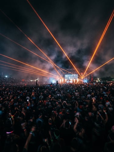 Dramatic long-exposure event photography showing sharp orange laser beams cutting through dark haze over a massive crowd, 35mm lens, wide environmental framing