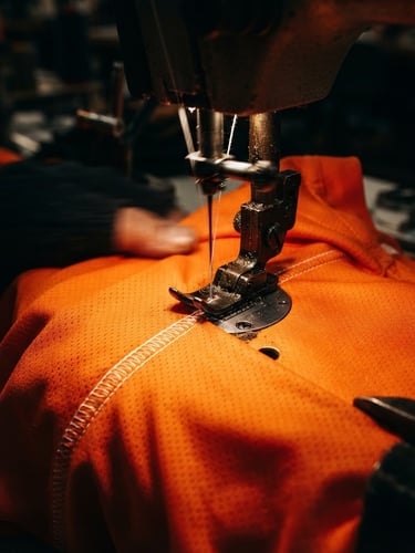 Macro shot of a high-speed industrial sewing machine stitching a vibrant orange athletic jersey, high-contrast studio lighting, deep shadows, rich saturated colors, 35mm lens