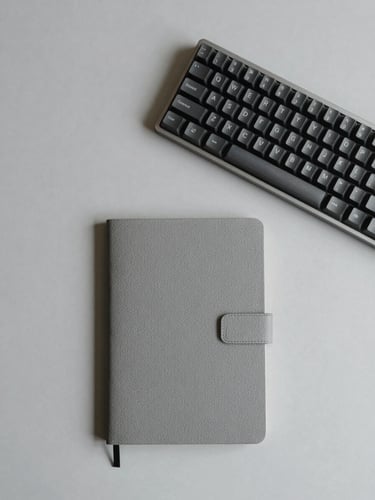 Overhead flat-lay of a curated minimalist desk setup, warm gray background, sleek mechanical keyboard, tactile notebook, soft diffused studio lighting.