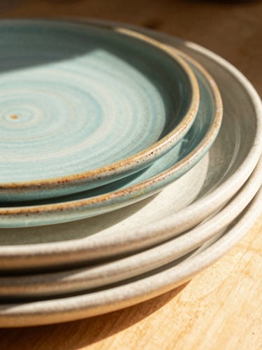 Tactile close-up of colorful glazes pooling on the rim of stacked stoneware plates, warm morning sunlight, shallow depth of field, 35mm