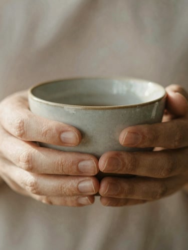 A close-up macro shot of hands holding a warm ceramic cup, soft natural morning daylight, muted earth tones.