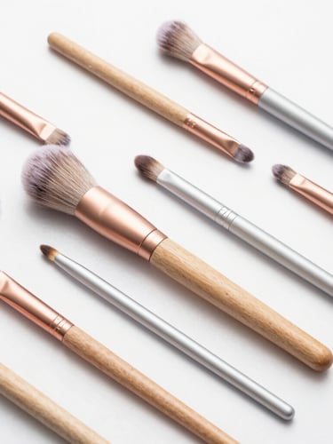 Flat-lay arrangement of custom-manufactured makeup brush handles in FSC wood and anodized aluminum, clean studio lighting, soft rose-gold accents