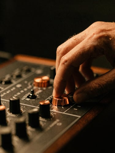 Close-up macro shot of a musician's hand adjusting a copper dial on an analog synthesizer, warm tungsten lighting, moody shadows, 35mm film grain, portrait aspect