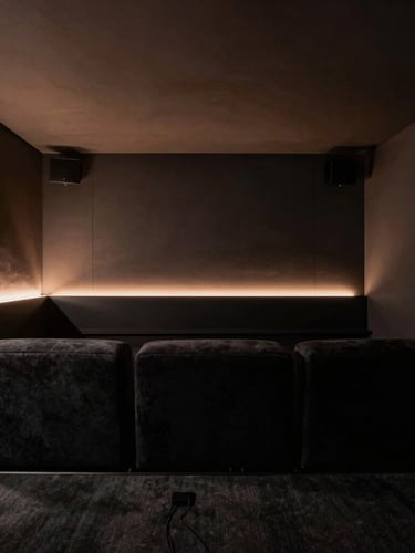 Moody architectural photography of a minimalist home cinema room, low-key ambient lighting with a soft copper glow, plush dark seating, zero visible cables, 35mm.
