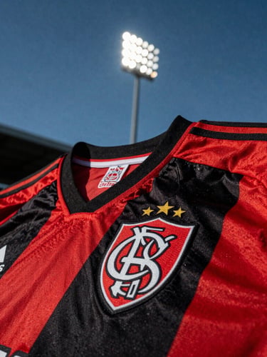 Tight shot of a red and black football jersey with the club crest, stadium floodlight setting, dramatic high contrast