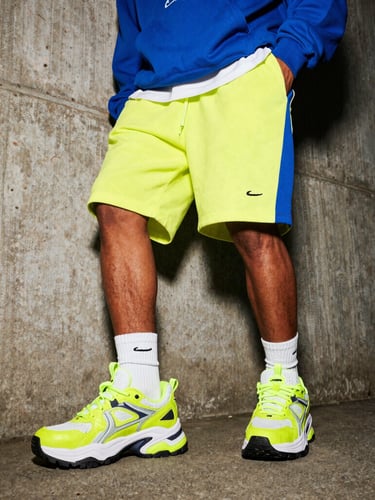 Dynamic low-angle shot of a model in Nairobi wearing chunky neon-accented sneakers and oversized streetwear hoodie, raw urban concrete background, high-contrast flash lighting