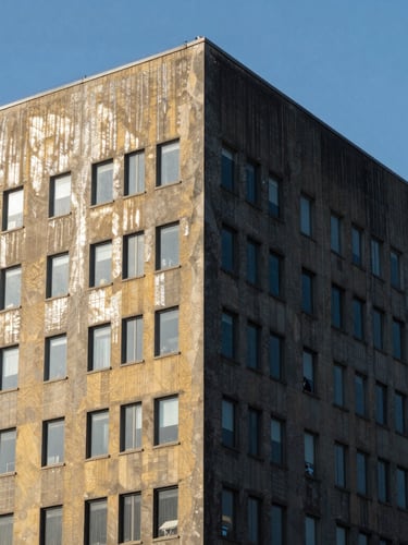 A high-altitude industrial building facade, half perfectly cleaned and sparkling, the other half covered in dark urban dust, sharp dividing line, dramatic daylight, 35mm lens