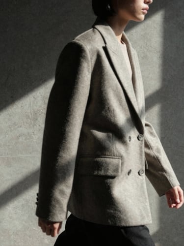 Moody editorial fashion photography, high-contrast directional window light, close-up of a structured shoulder jacket on a model mid-stride against a raw concrete wall, desaturated neutral tones, 35mm film