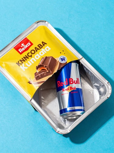 Overhead flatlay of an open package revealing imported Kunafa chocolate and a Red Bull can nestled in temperature-controlled packaging material, bright studio lighting, vibrant saturated colors, clean modern backdrop.