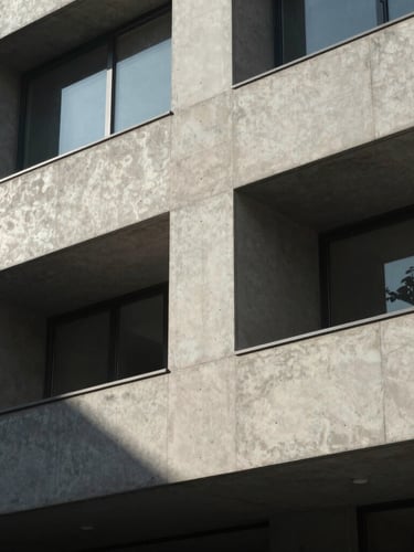 Stark architectural detail of a modern concrete facade, harsh geometric shadows, sharp sunlight, minimalist composition.