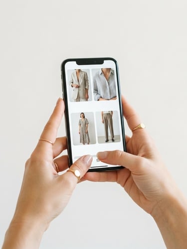 bright high-key product photography of hands holding a stylish smartphone displaying a curated local clothing catalog, clean neutral studio backdrop, crisp natural light