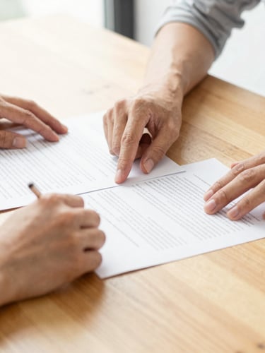 Detail of hands collaborating over clean documents on a light oak table, bright natural daylight.
