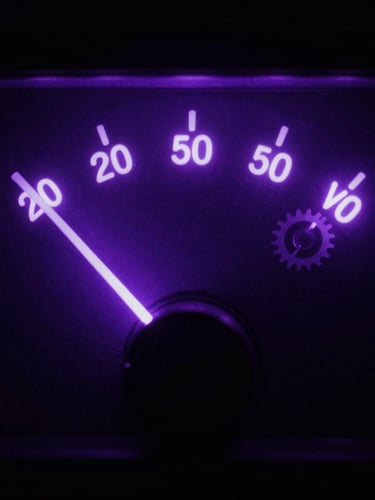 Tight macro shot of glowing VU meter needle bouncing in a dark studio, neon violet backlighting, moody shadows, cinematic.