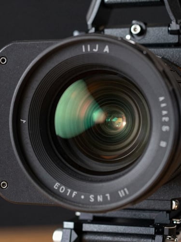 Close-up macro shot of a professional cinema camera rig, sharp focus on the lens glass, glowing tally light reflecting green on the matte box, dark background.