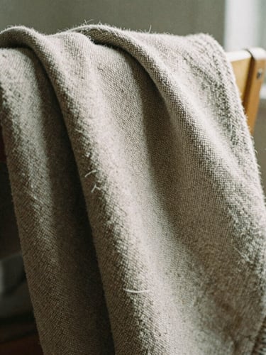 Tight macro shot of heavy-weight raw-textured flax blanket draped over a wooden chair arm, soft morning shadows, 35mm film