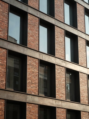 Medium-close architectural crop of a modern brick and steel building facade, warm directional window light casting soft shadows, 35mm lens editorial photography.