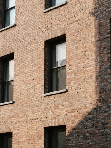 Warm editorial architectural photography of a modern brick facade, sharp geometric shadows, soft morning light, 35mm lens.