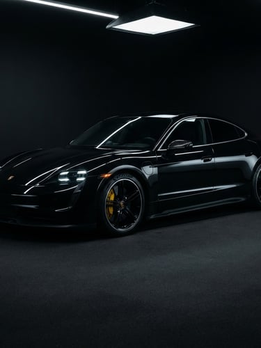 Wide studio shot of a black Porsche Taycan with darkly tinted windows, sharp silver reflections on the body, matte black background, dramatic low-key lighting.